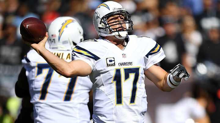 A football player in a white jersey with the name 'Chargers' throwing a football during a game.