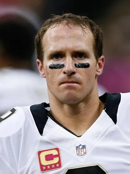 Close-up of a football player wearing a white jersey with a captain's patch, with black eye paint under his eyes, looking serious.