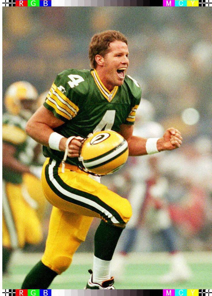 A football player in a green and yellow jersey celebrates on the field, holding a football while showing intense emotion.