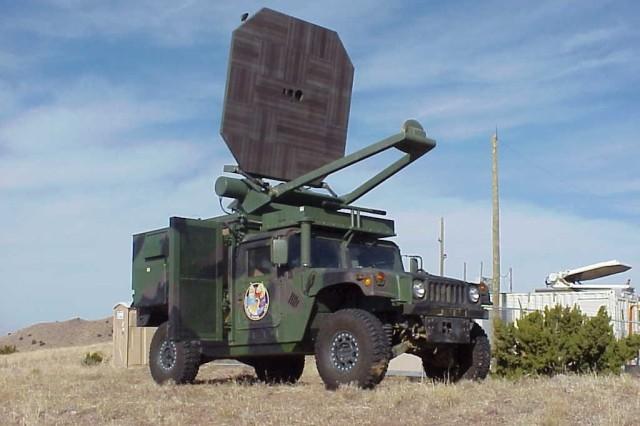 Military vehicle equipped with a large radar system, set against a clear blue sky.