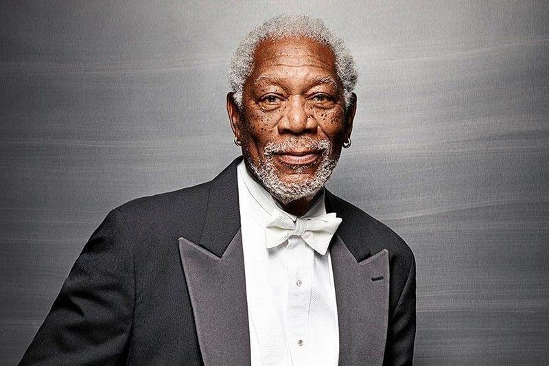 A distinguished older man with gray hair, wearing a tuxedo and a bow tie, smiling against a textured gray background.